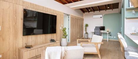 A modern living room with a large flat-screen TV, wooden flooring, and a ceiling with exposed beams.