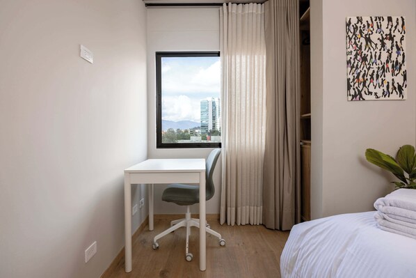 Une chambre d’hôtel équipée d’un bureau, d’un lit, d’une fenêtre avec des rideaux et offrant une vue sur la ville.