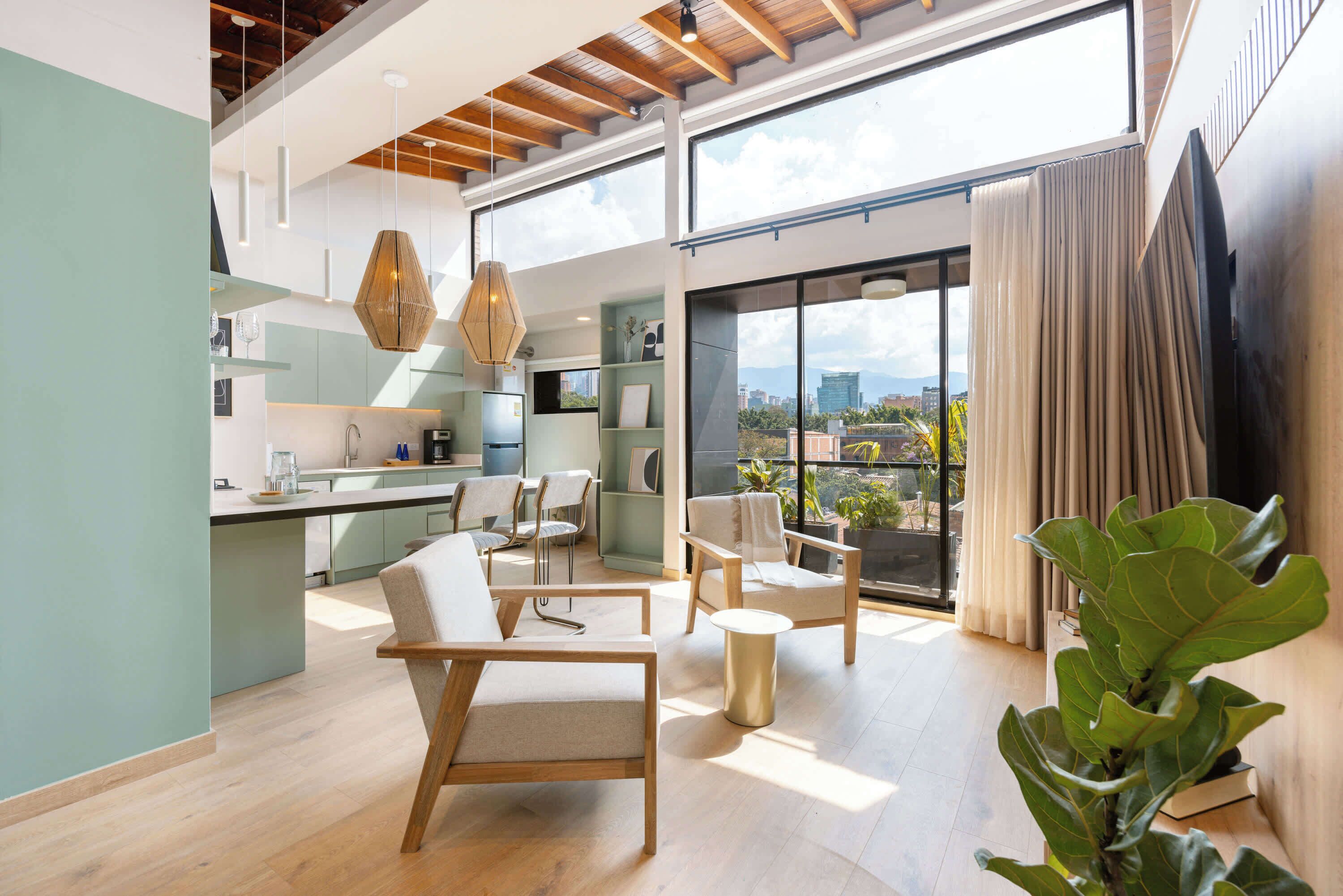Amplia sala de estar con cocina, comedor y ventanas grandes que ofrecen vistas a la ciudad.