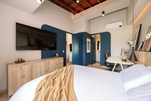 A modern bedroom with a large bed, a desk, and a chair. There is a wardrobe and a mirror on the wall.