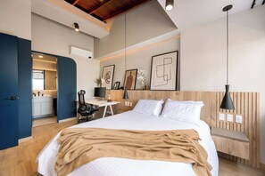 Quarto moderno com cama grande, escrivaninha e cadeira. É visível um banheiro ao fundo.