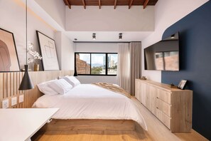 Een moderne slaapkamer met een groot bed, een houten hoofdbord, een bureau en een aan de muur bevestigde televisie.