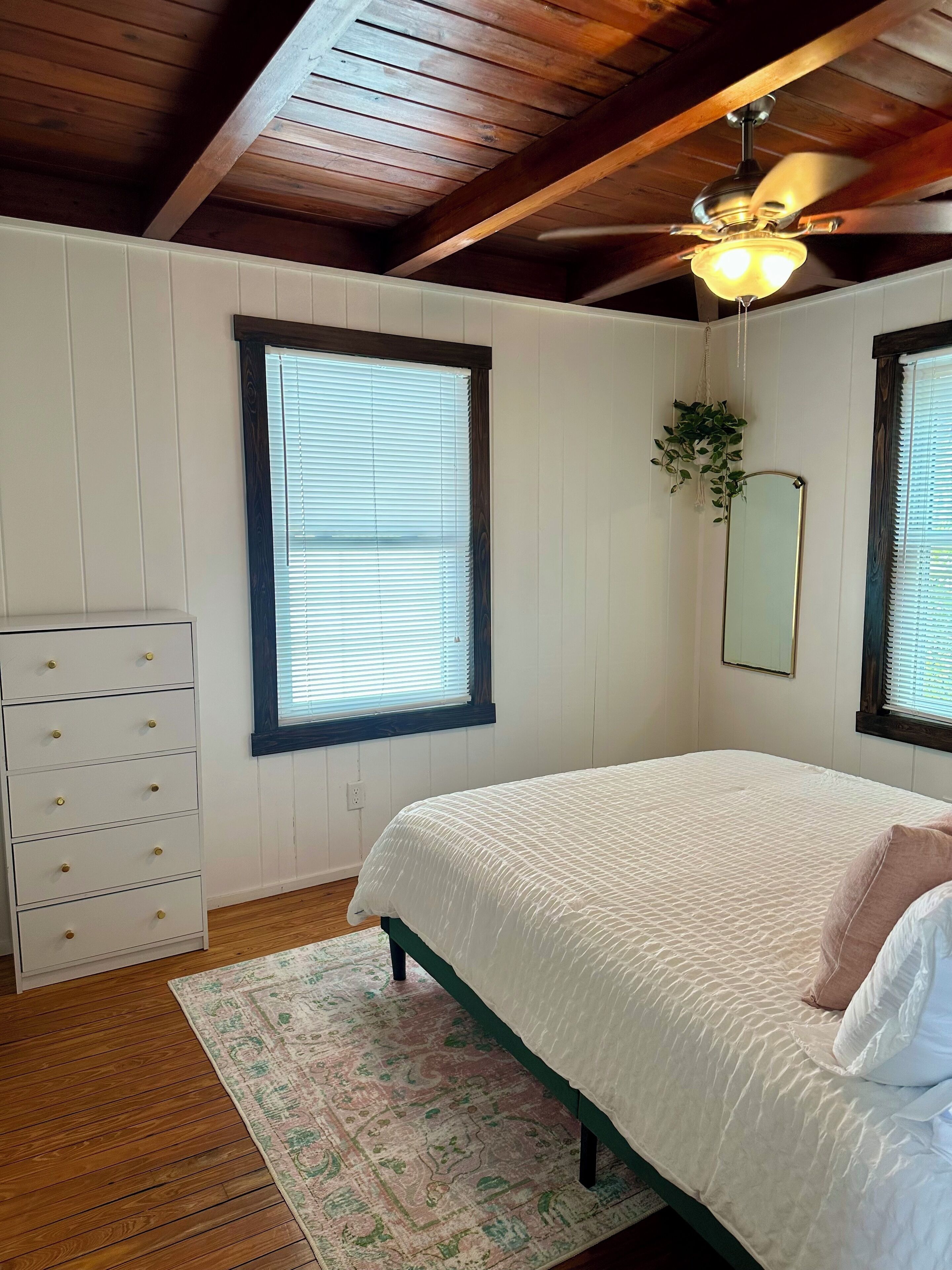 Ein Schlafzimmer mit Bett, Kommode, Deckenventilator und einem Fenster mit Jalousien.