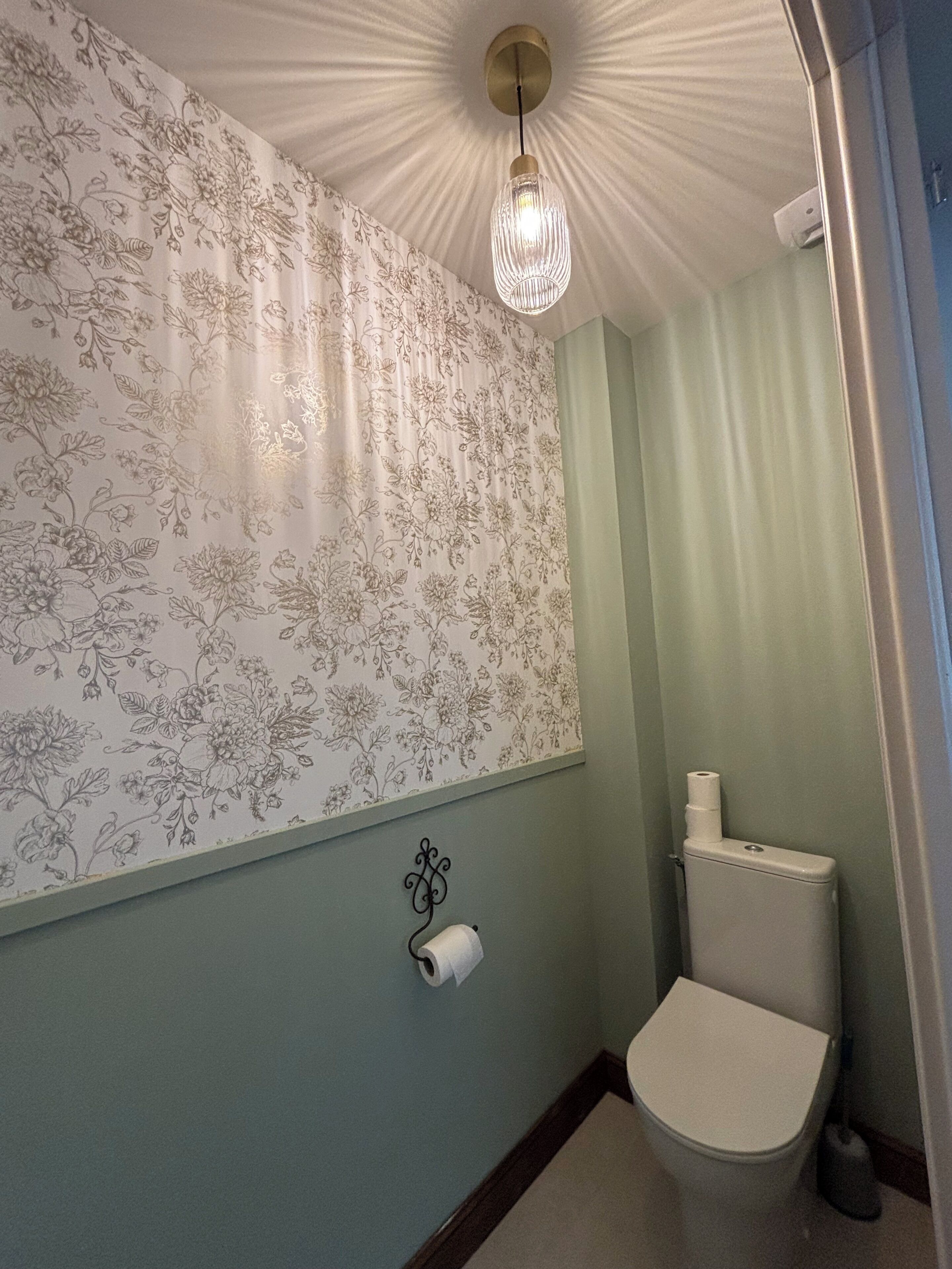 A bathroom with floral wallpaper, a toilet, and a hanging light fixture.