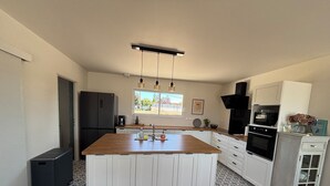 A modern kitchen with white cabinets, a wooden island, a black refrigerator, and a window providing natural light. - La vigne" house in the countryside near Sarlat with beautiful view! (Marcillac-Saint-Quentin)