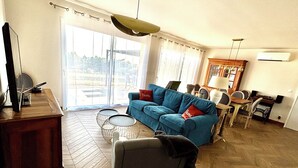 A living room with a blue sofa, a wooden coffee table, and a dining area with a table and chairs. - La vigne" house in the countryside near Sarlat with beautiful view! (Marcillac-Saint-Quentin)