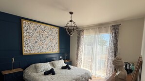 A bedroom with a large bed, a nightstand, a dresser, a chandelier, and a large floral artwork on the wall. - La vigne" house in the countryside near Sarlat with beautiful view! (Marcillac-Saint-Quentin)