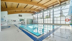 Piscina interna com teto de madeira, paredes de vidro transparente e piso revestido de azulejos.
