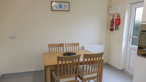 Uma área de refeições com uma mesa de madeira e quatro cadeiras, uma obra de arte emoldurada na parede e um aviso de segurança contra incêndio.
