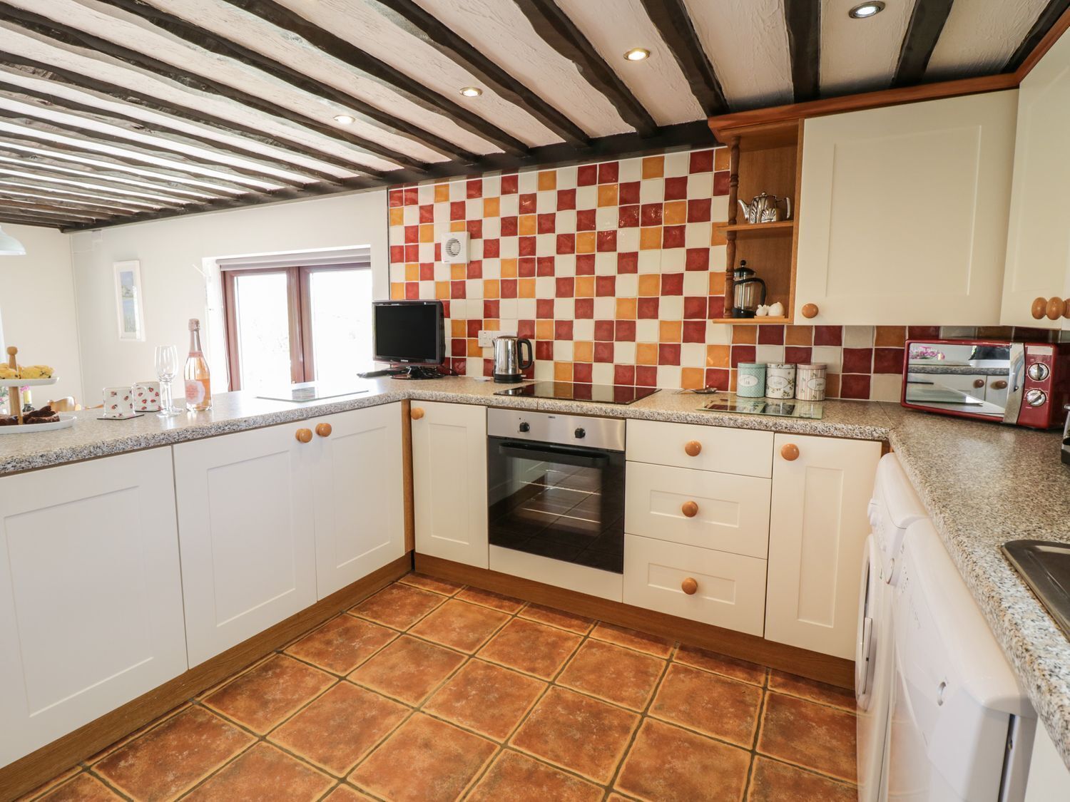 A kitchen with white cabinets, a tiled backsplash, a built-in oven, and a red toaster.