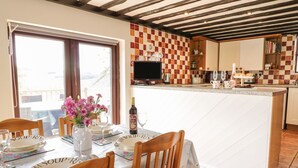 Un comedor con una mesa dispuesta para cuatro, una cocina con baldosas de cuadros y un balcón visible a través de la ventana.