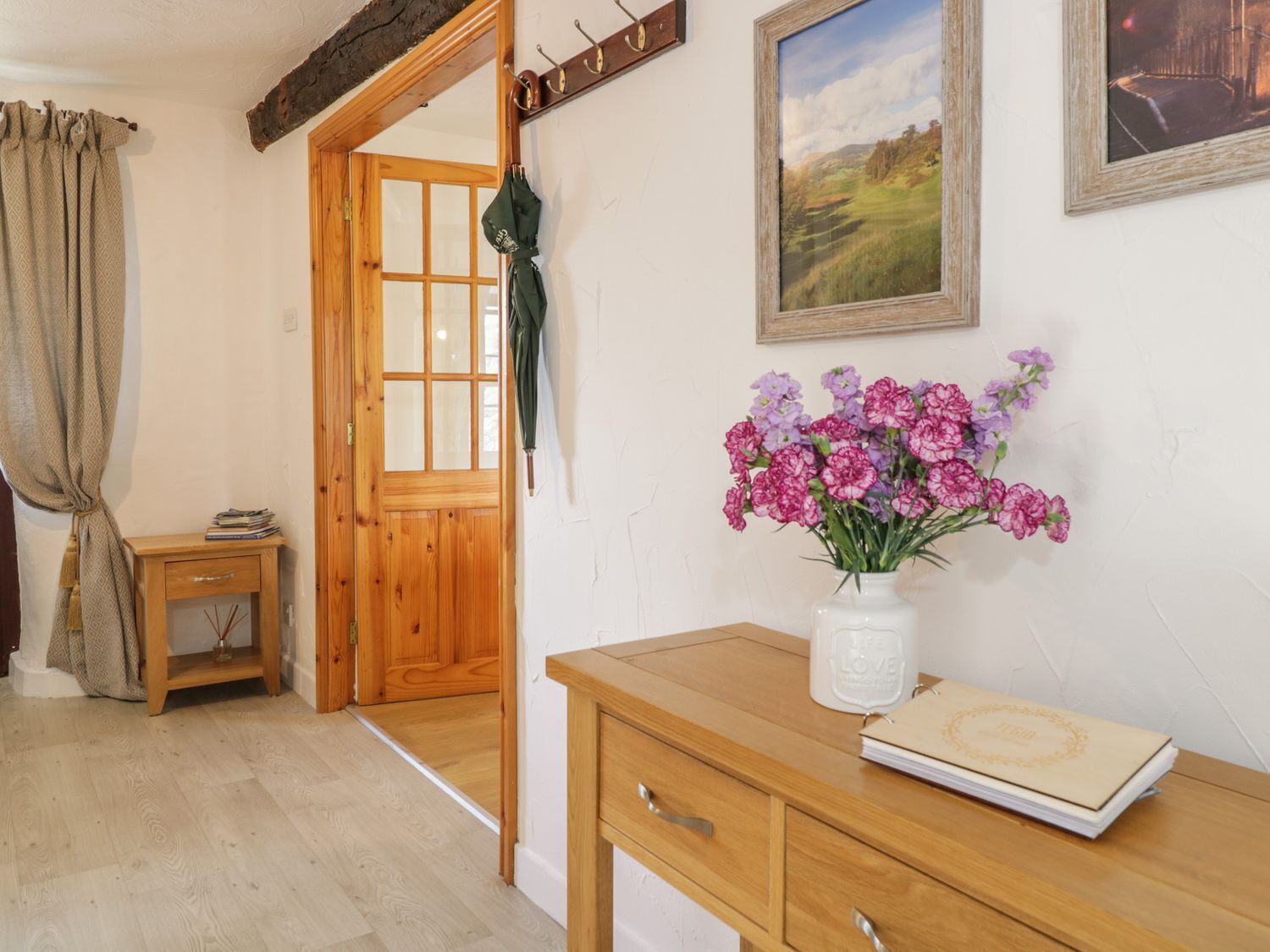 A wooden desk with a vase of flowers, a framed landscape painting, and a wooden door leading to another room.