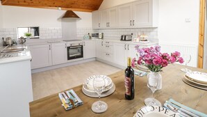 A modern kitchen with white cabinetry, a wooden ceiling, and a dining area set for a meal. - Cyffdy Cottage - Tegid (Bala)