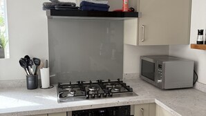 A kitchen with a gas stove, oven, microwave, and a countertop with kitchen utensils. - Mostyn View (Wirral)