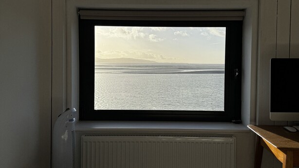 A room with a view of a calm sea and distant mountains through a window. - Mostyn View (Wirral)