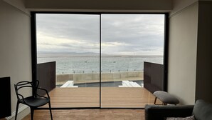 A room with a large sliding glass door leading to a wooden deck overlooking a body of water. - Mostyn View (Wirral)