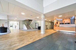 Een ruime lobby met een houten vloer, een receptiebalie, een trap en een wachtruimte met een bord.