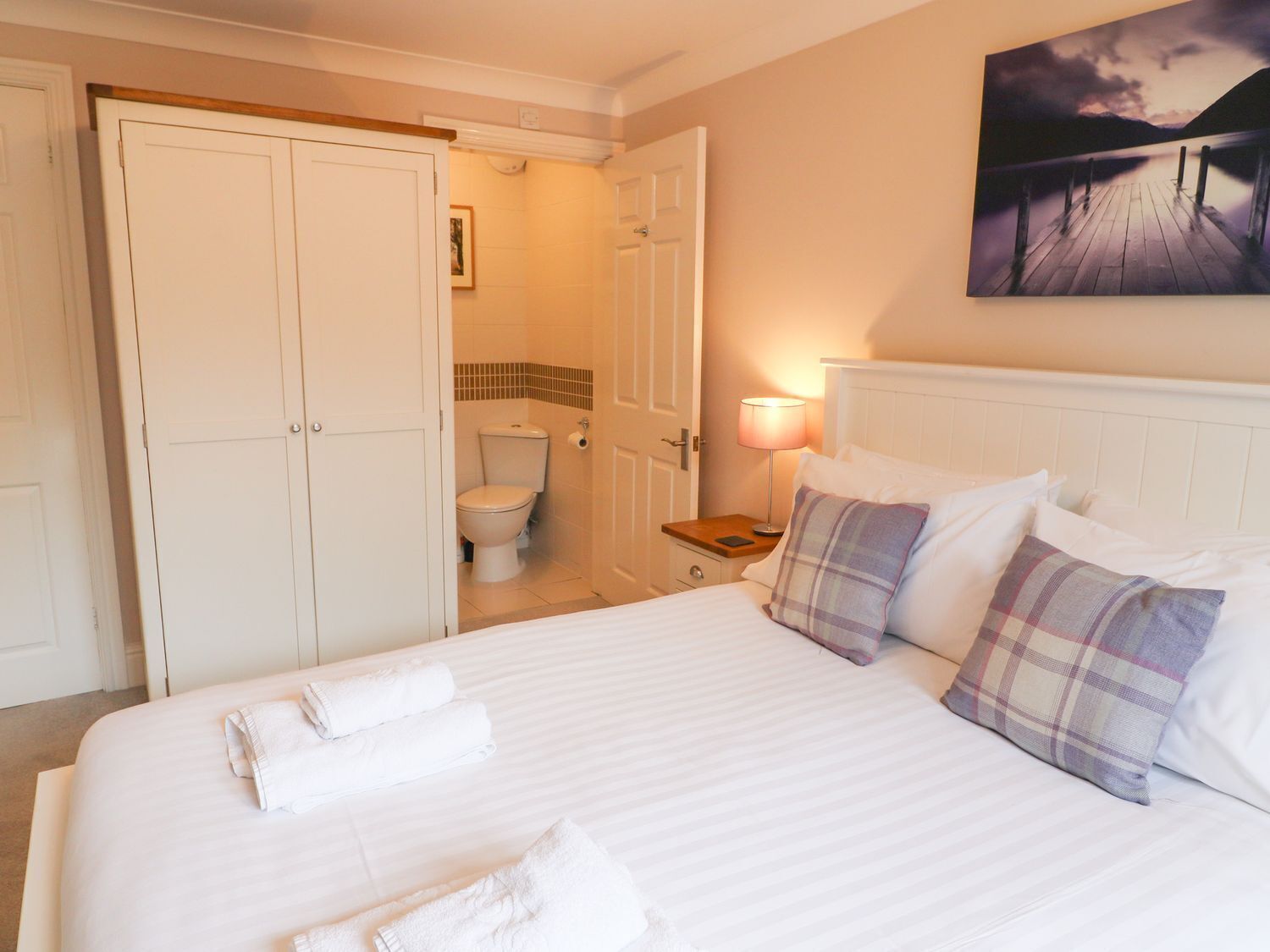 A hotel room with a bed, a nightstand, a painting, and a bathroom visible through an open door.