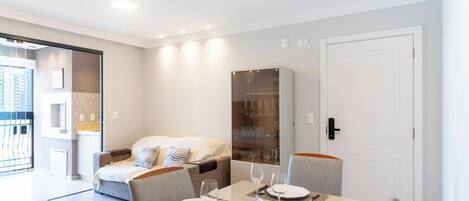 A modern hotel room with a dining area, a bed, and a glass cabinet.