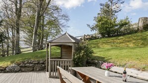 Um deck de madeira com mesas e bancos de piquenique, uma pequena construção de madeira e um muro de pedra.