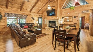 Un intérieur de chalet chaleureux avec une cheminée, un plancher en bois, un canapé en cuir et un coin repas.