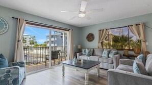 A spacious living room with a large sliding glass door to the outside, a ceiling fan, and a view of the surrounding buildings.