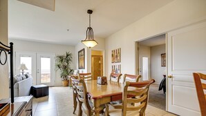 A dining area with a wooden table and chairs, a hanging light fixture, and a potted plant. - Golf Course Views & Private Deck: Mesquite Condo! (Mesquite)