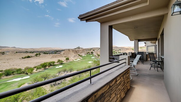 A balcony with a stone wall, a view of a golf course, and a seating area with chairs and a table. - Golf Course Views & Private Deck: Mesquite Condo! (Mesquite)