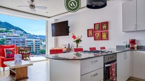 A modern kitchen with a central island, white cabinets, and a large window offering a city view. - The Park 506 | 2BR/2BA | Puerto Vallarta | Pool, Gym (Puerto Vallarta)