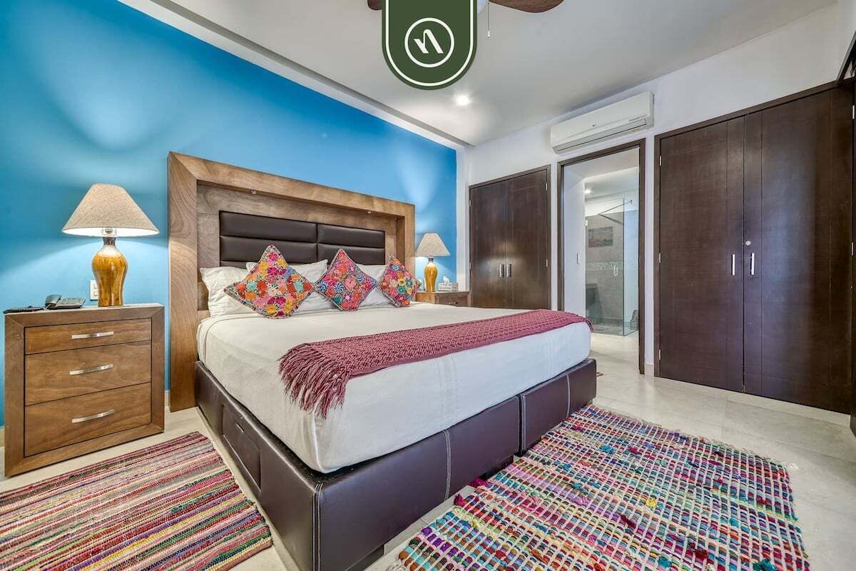 Ein Schlafzimmer mit einem großen Bett, zwei Nachttischen, einem Kleiderschrank und einem durch eine offene Tür einsehbaren Badezimmer.