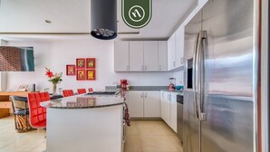 A modern kitchen with white cabinets, a stainless steel refrigerator, a granite countertop island, and a dining area with red chairs. - The Park 506 | 2BR/2BA | Puerto Vallarta | Pool, Gym (Puerto Vallarta)