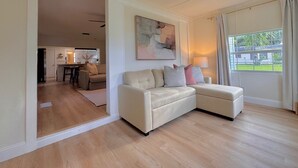 A modern living room with a beige sectional sofa, a dining area, and a kitchen visible through an open door. - Blue Cottage On Parker- by CasaDuran (Lakeland)