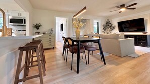 A modern kitchen with a microwave, stove, and wooden stools. There is a dining table with chairs and a sofa in the living area. - Blue Cottage On Parker- by CasaDuran (Lakeland)