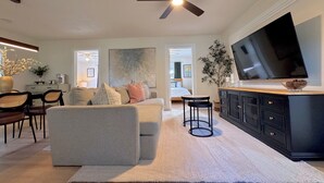 A modern living room with a grey sofa, a coffee table, a TV, and a ceiling fan. - Blue Cottage On Parker- by CasaDuran (Lakeland)