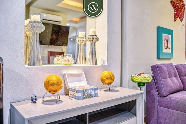 A modern interior with a light-colored console table displaying decorative items, a purple sofa, and a mirror reflecting the room.