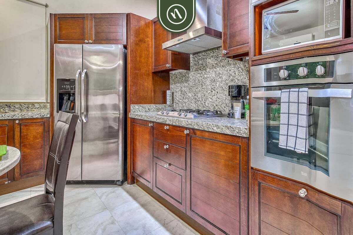 A kitchen with a stainless steel refrigerator, wooden cabinets, granite countertops, and a built-in oven.