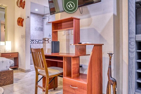 A compact room with a wooden desk, a chair, a television mounted on the wall, and a small shelf with decorative items. - V399 108 | 1BR/1BA Puerto Vallarta | Near Ocean, Pool, Rooftop (Puerto Vallarta)