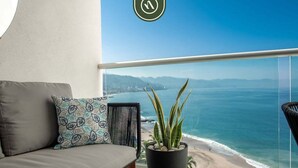 A balcony with a sofa, a potted plant, and a view of the ocean and mountains.
