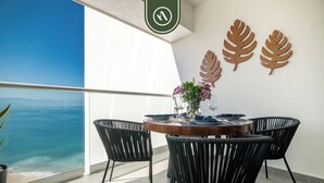 A balcony with a view of the ocean, a round table with chairs, and decorative leaf wall art.