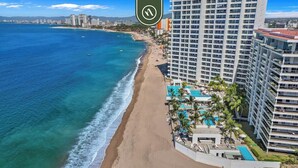 A coastal hotel with a beach view, multiple swimming pools, and high-rise buildings in the background.