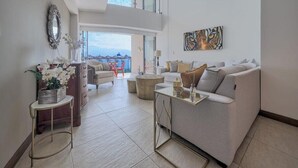 A modern living room with a sofa, coffee table, and decorative items. There is a view of the outdoors through large windows. - Luxury 2BR Condo in Marina - Pool - Zen Rooftop (Puerto Vallarta)
