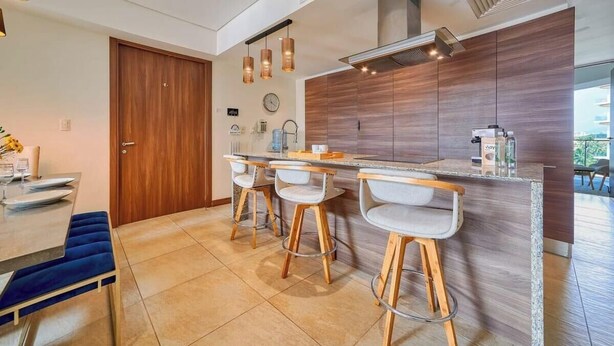 Eine moderne Küche mit Holztür, einer Bar inklusive Sitzhocker und einem Esstisch mit Stühlen.