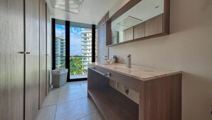 A modern bathroom with a large mirror, wooden cabinets, and a view of a high-rise building. - Luxury 2BR Condo in Marina - Pool - Zen Rooftop (Puerto Vallarta)