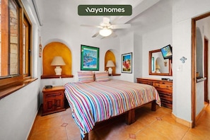 A bedroom with a bed, two bedside tables, a ceiling fan, and framed pictures on the wall.