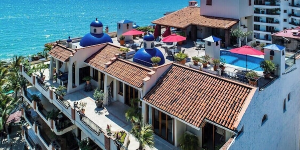 A hotel with a rooftop pool, blue domed structures, and a view of the sea.