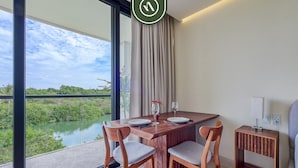 A modern room with a wooden dining table, two chairs, a side table, and a view of a water body.