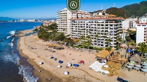 Ein Hotel direkt am Strand mit mehreren Balkonen, einem Sandstrand und Sonnenschirmen.