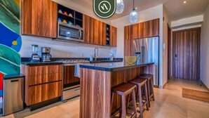 Una cocina moderna con armarios de madera, una isla central con taburetes, electrodomésticos de acero inoxidable e iluminación colgante.