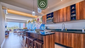 Una cocina moderna con armarios de madera, una isla central con taburetes, un microondas y un mural colorido en la pared.