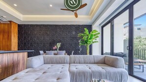 A modern living room with a sectional sofa, a wooden cabinet, a black textured wall, and a ceiling fan. - Amazing 1 BR Condo with Terrace - Rooftop Pool (Puerto Vallarta)